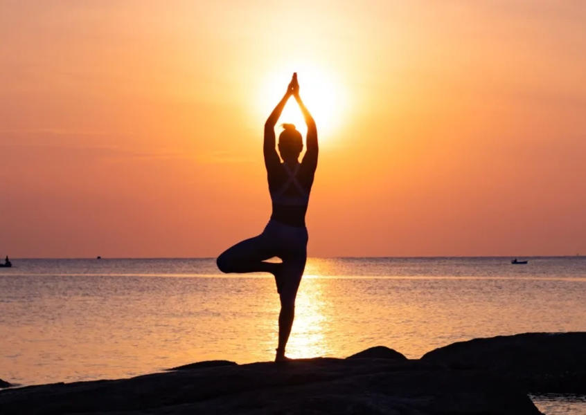 Silhouette of a woman performing Vrksasana tree pose yoga at sunset on the beach at Anantara Quy Nhon Villas