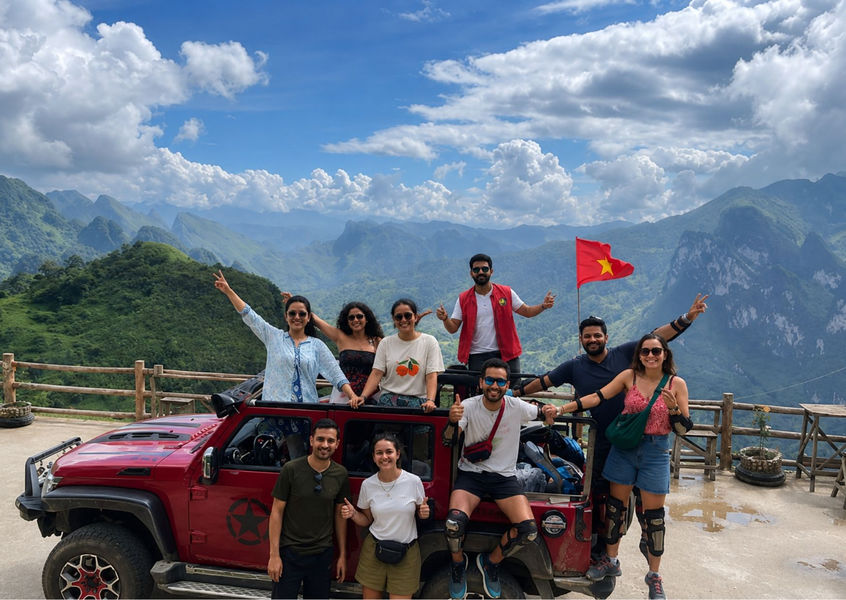 Group posing with a red jeep at a mountain viewpoint overlooking the Ha Giang Loop