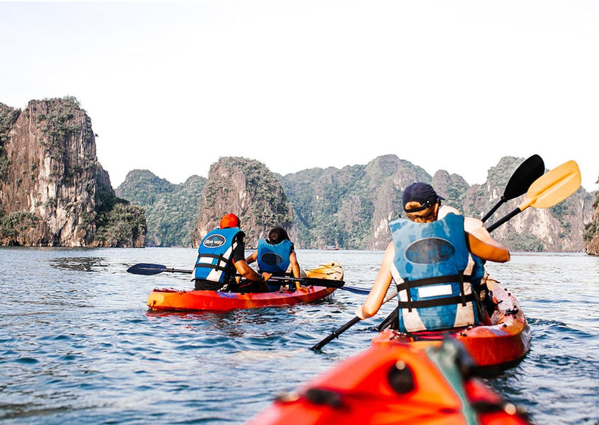 Kayakers paddling among limestone cliffs in the calm waters of Ha Long Bay