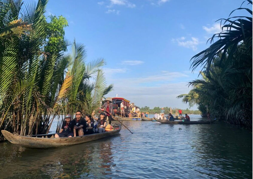 Tourists riding traditional wooden boats along a palm-lined canal in the Mekong Delta