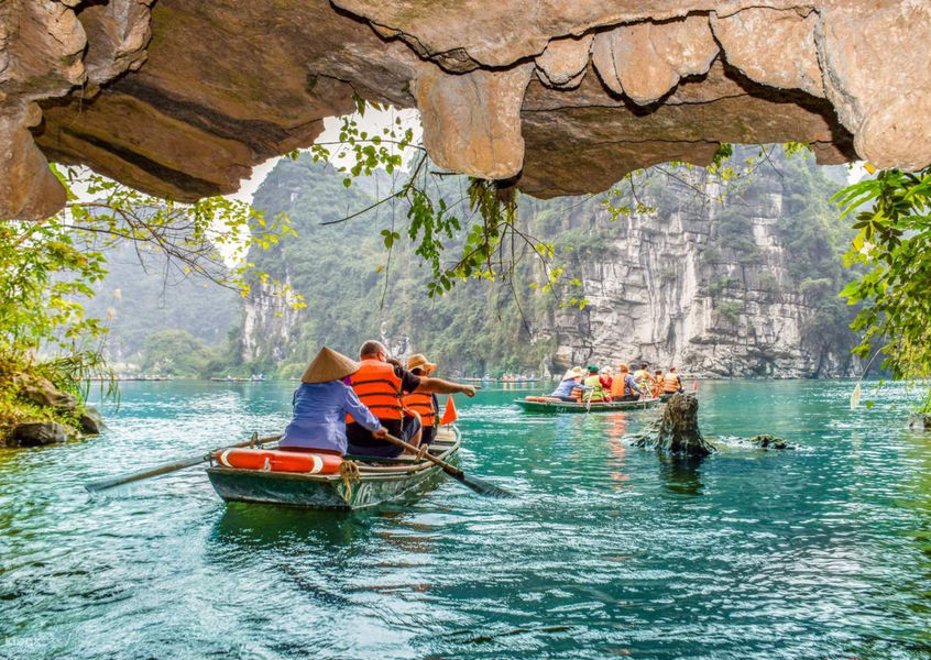 Tourists rowing wooden boats through a limestone cave passage in Trang An, Ninh Binh