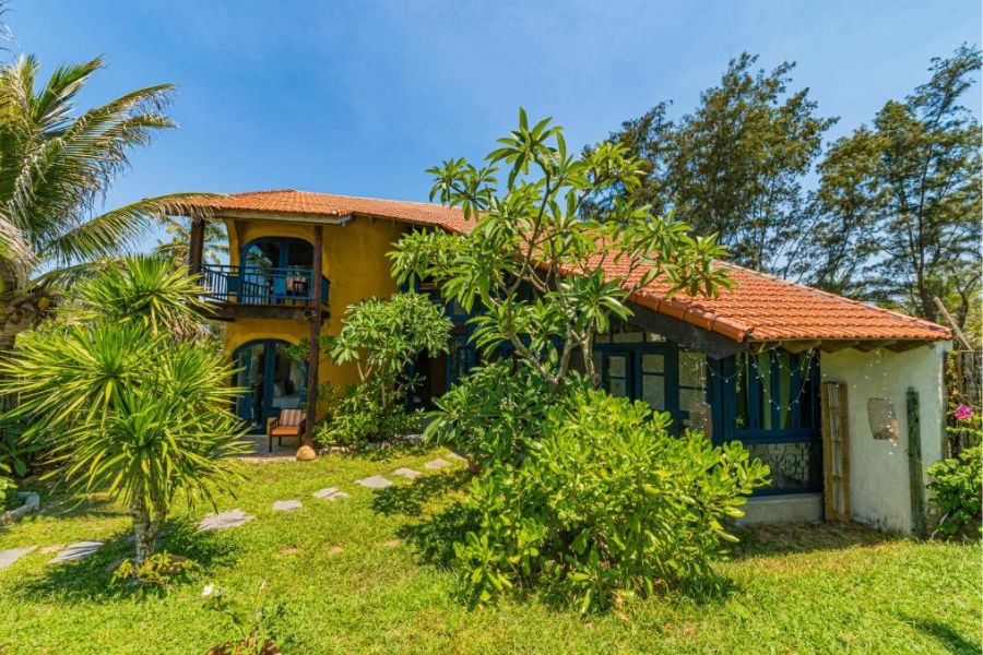 Yellow two story villa with red tile roof and tropical garden