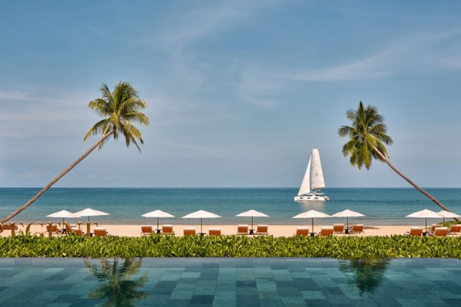 Infinity pool overlooking beach with palm trees and sailboat