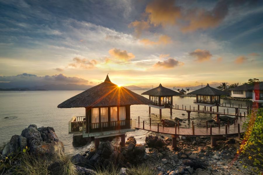 Overwater thatched-roof villas connected by a wooden walkway at sunrise on Hon Tre Island