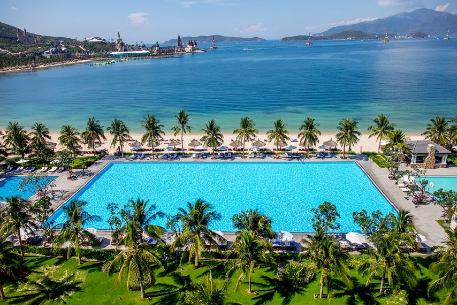 Large resort swimming pool along a palm-lined beach with the Nha Trang skyline in the background