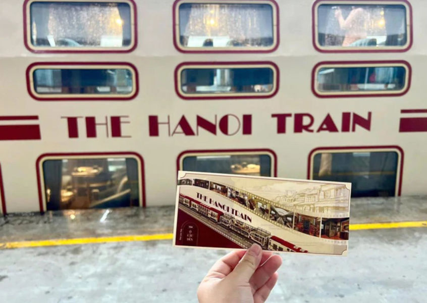 Hand holding a paper ticket in front of The Hanoi Train