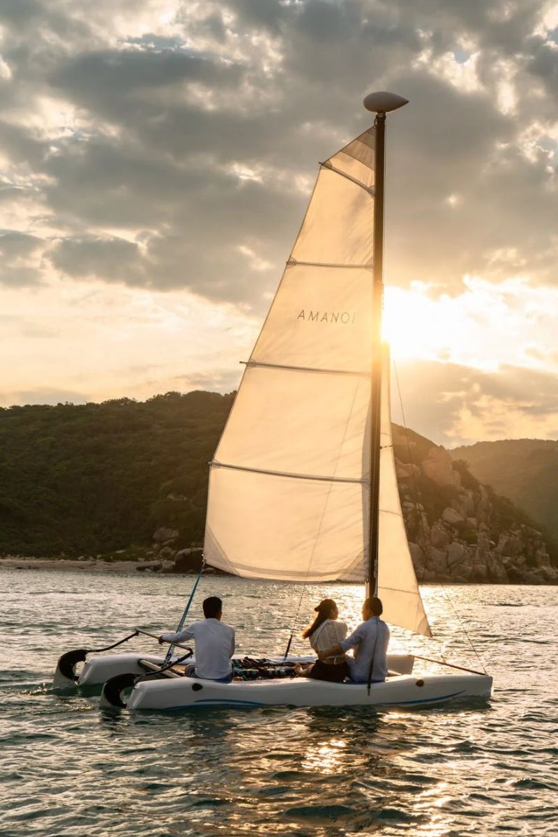 Sailing a catamaran at sunset beside a forested coastline at Amanoi, Vietnam